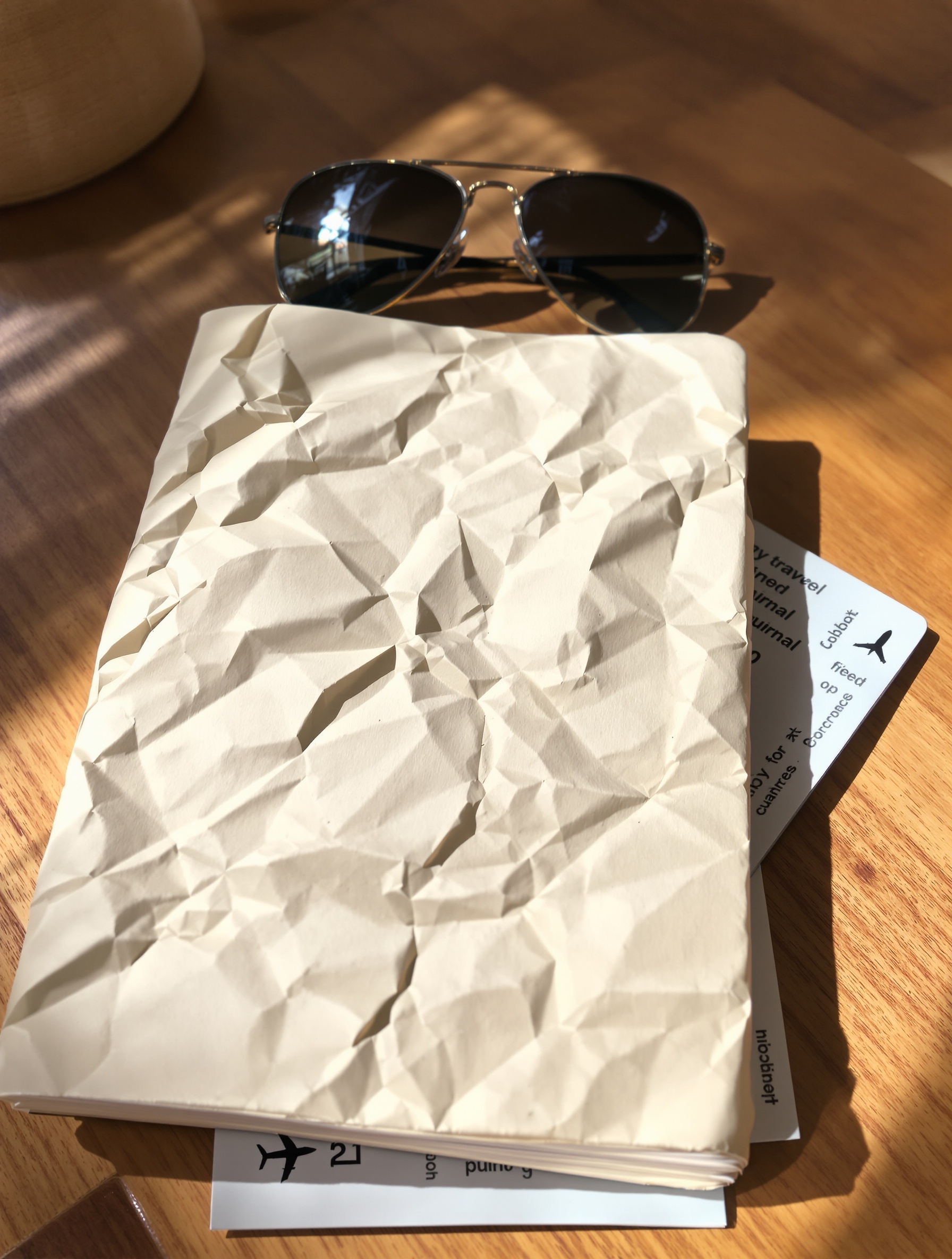 Carnet de voyage froissé, lunettes de soleil et billets d'avion sur une table en bois, ambiance décontractée