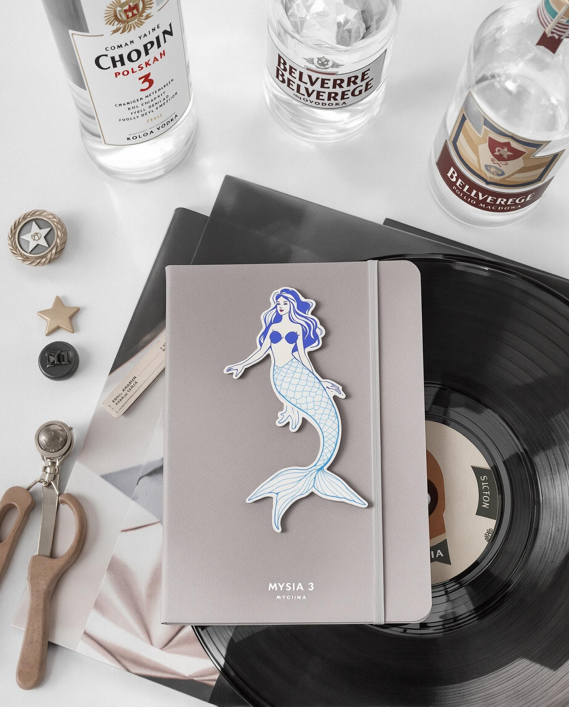 Magnet kitsch sirène, carnet Mysia 3 design, badge vintage Kolo et bouteilles vodka Chopin/Belvedere sur fond lumineux hipster.