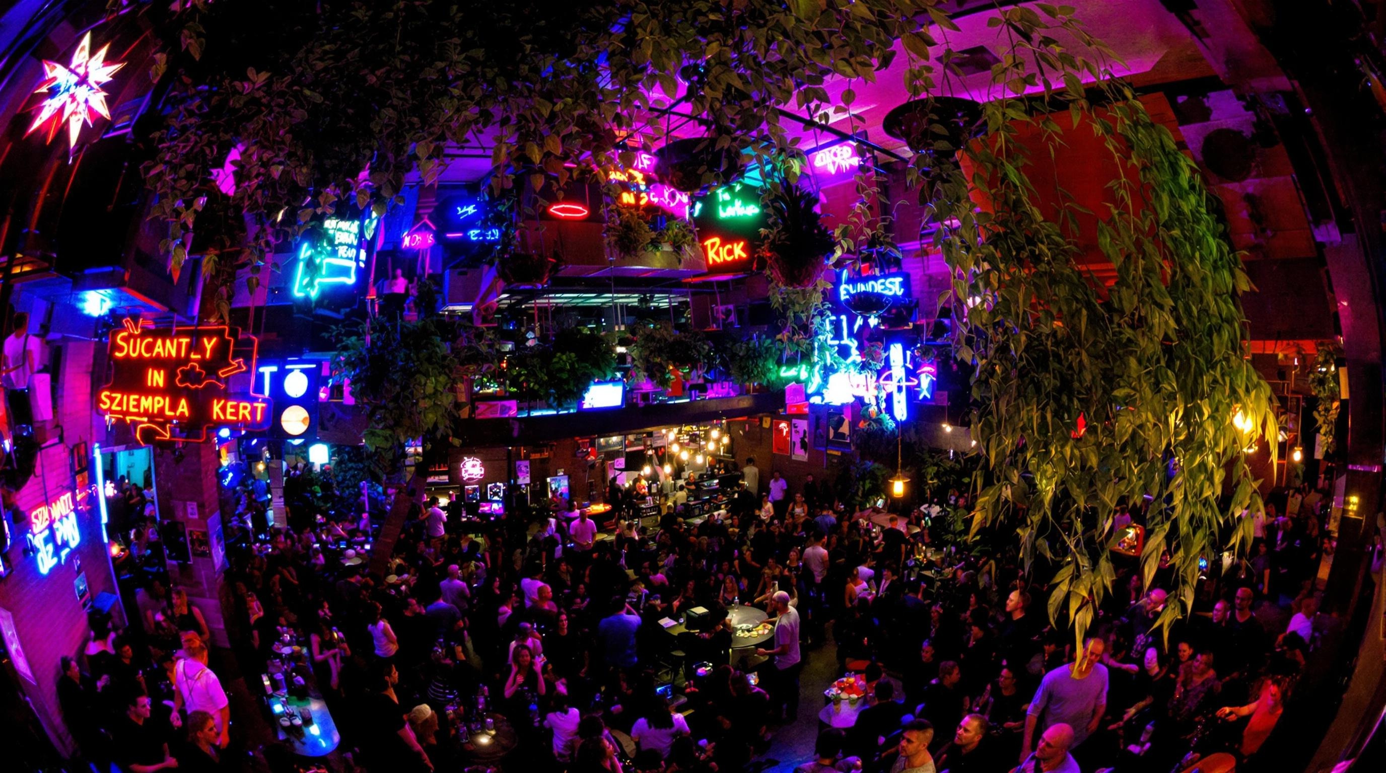 Vue nocturne du décor éclectique de Szimpla Kert avec néons et plantes suspendues, foule internationale au rez-de-chaussée