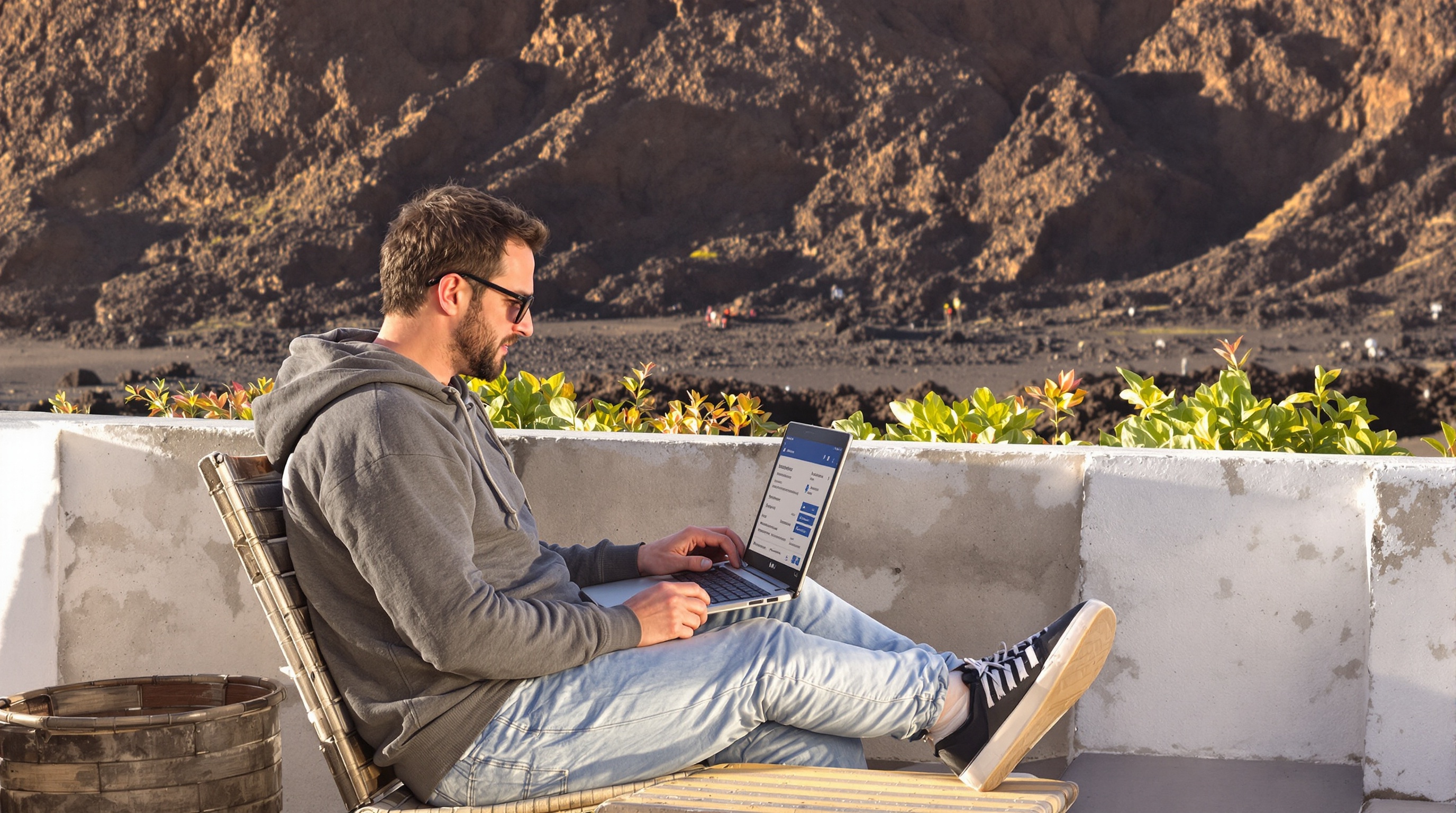 Voyageur sur terrasse déserte à Lanzarote en octobre, laptop ouvert et paysage volcanique sous lumière dorée.