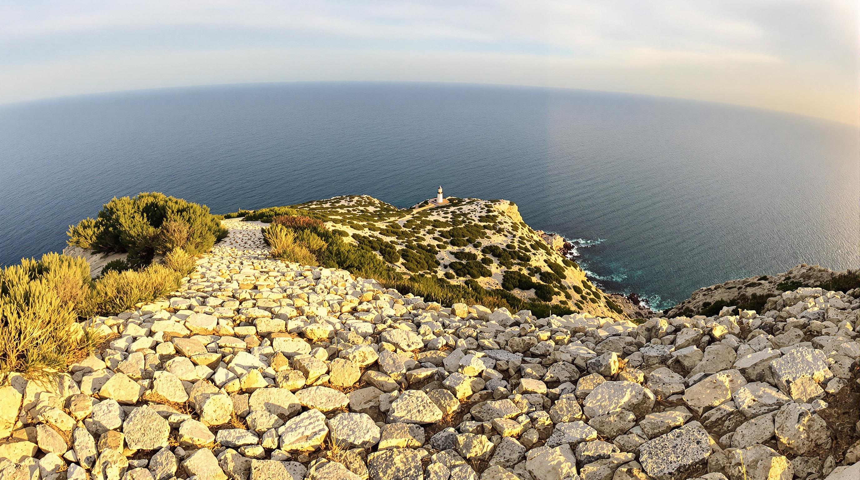 Vue panoramique sur la Méditerranée et le Phare du Cap d’Arme, avec un sentier rocailleux au premier plan.