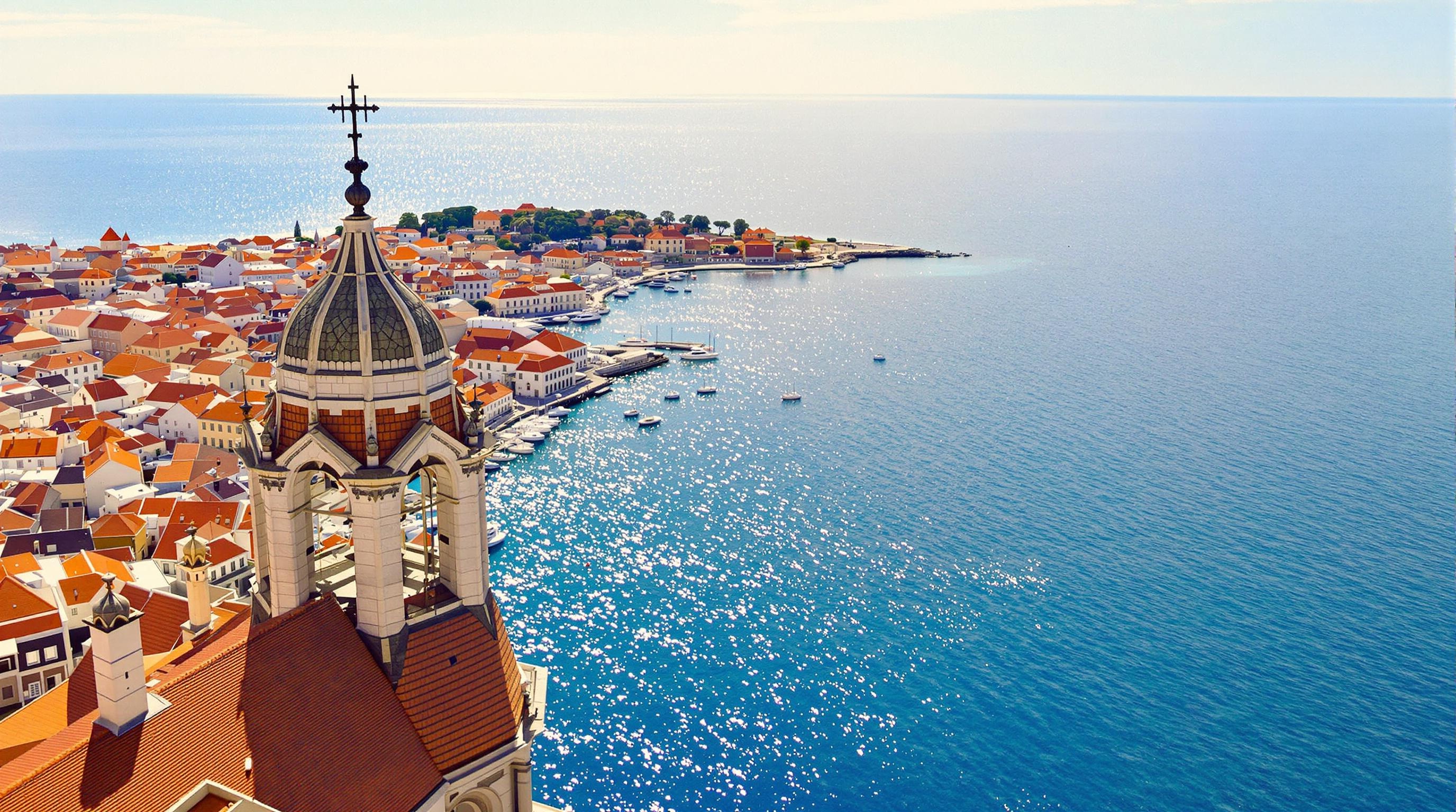 Vue plongeante depuis le clocher de la Cathédrale Sainte-Anastasie avec la mer Adriatique en arrière-plan et les toits ocres de Zadar à la lumière dorée.